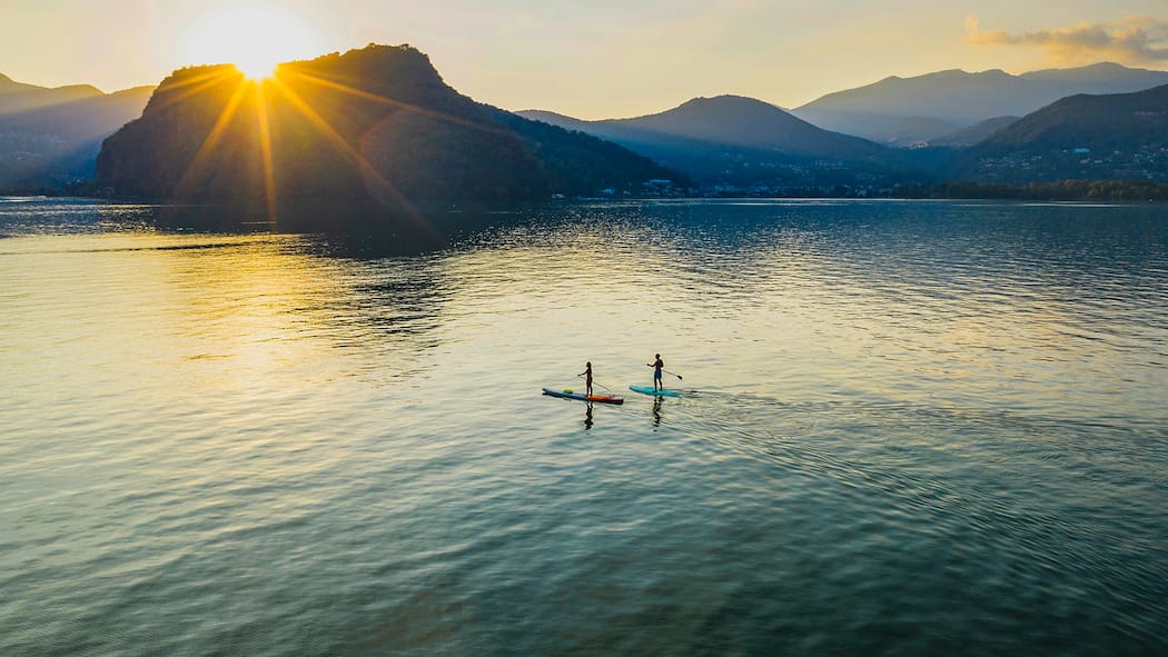 Fit bleiben mit kühlem Kopf Zwei Stand-Up-Paddler:innen auf dem Luganersee – kurz vor Sonnenuntergang