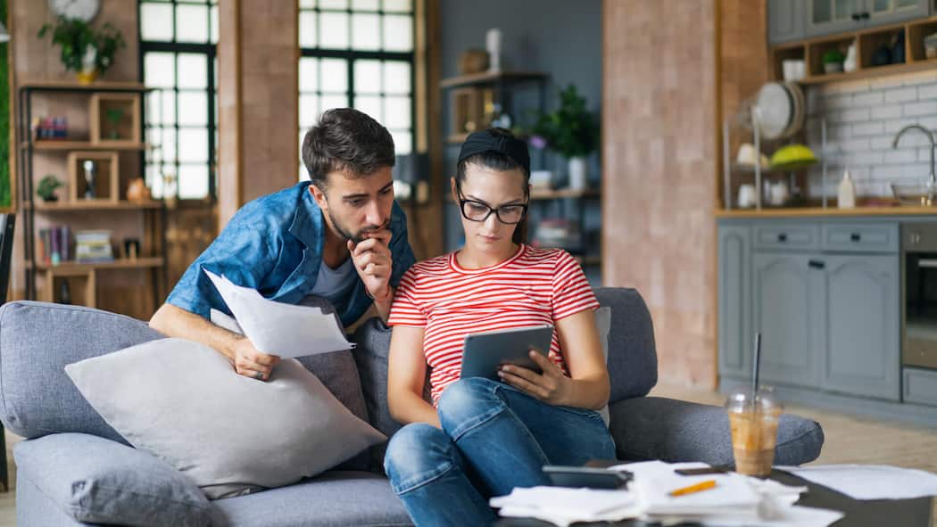 So füllen Sie Beitragslücken in Ihrer Vorsorge am sinnvollsten auf Couple calculating bills at home using laptop and calculator. Young couple working on computer while calculating finances sitting on couch. Young man with wife at home analyzing their finance with documents.1414921475