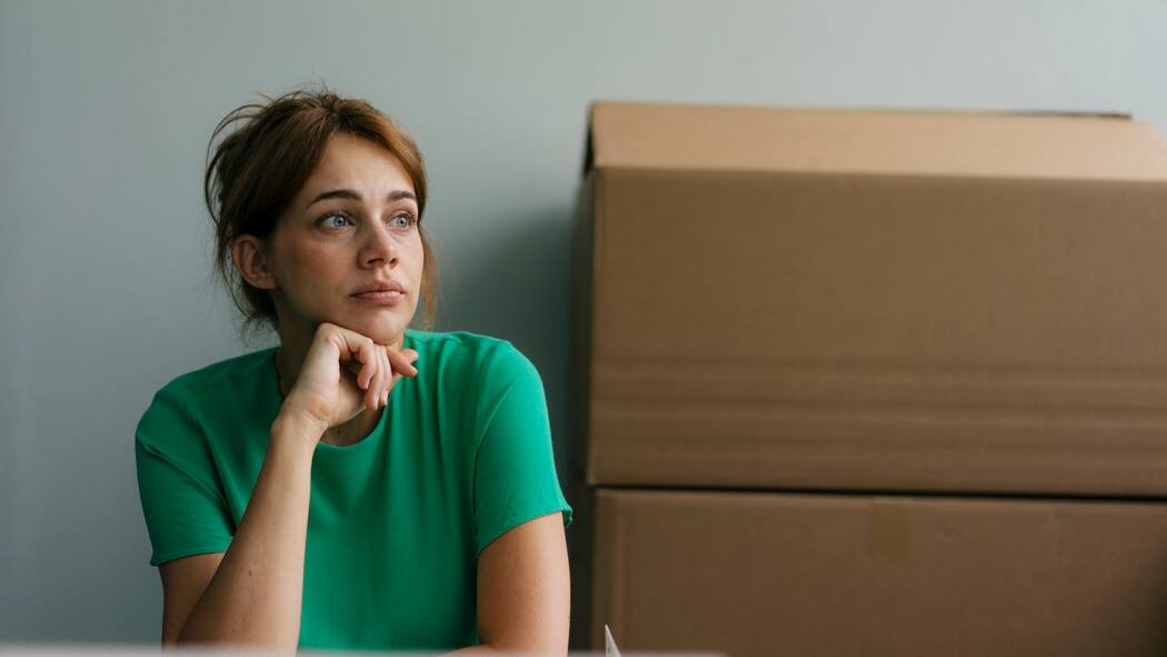 Wer die Miete nicht zahlt, fliegt raus Mieterin sitzt neben ihren Umzugskartons und schaut traurig.