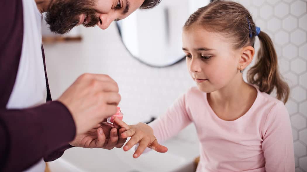 Alternierende Obhut – wie teilen wir den Unterhalt fair? Ein kleines Mädchen hat ihre rechte Hand ausgestreckt, damit ihr Vater die Nägel lackieren kann.