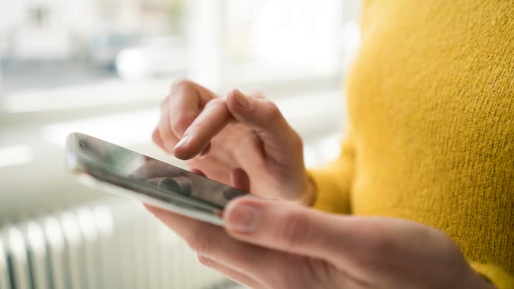 8 Tipps für kürzere Ladezeiten Eine Frau, deren Gesicht man nicht sieht, und die einen gelben Pullover trägt, tippt auf den Bildschirm eines Smartphones.