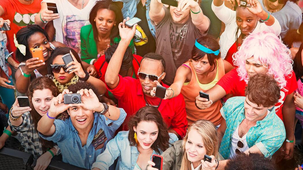 Jedes Foto ist geschützt Eine Gruppe junger Menschen steht in einer Masse zusammen und alle halten ein Handy oder eine Digitalkamera in die Höhe.