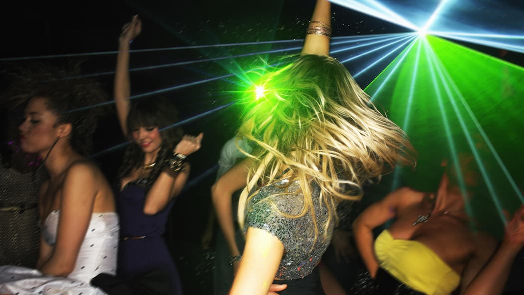 Wenn Teenies ins Nachtleben wollen – was können Eltern tun? Eine Gruppe Frauen tanzt vor grünem Club-Licht. Wenn Jugendliche in den Ausgang wollen, sollten Eltern klare Regeln festlegen.