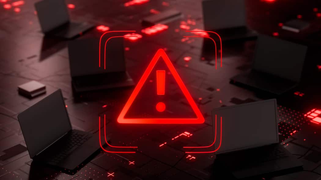 Bund verschläft IT – unsere sensiblen Daten sind in Gefahr Futuristic cybersecurity warning concept featuring a glowing red alert symbol surrounded by laptops on a dark digital circuit board. The image represents an anonymous hacker attack, cybercrime, malicious software, malware infection, ransomware, phish…