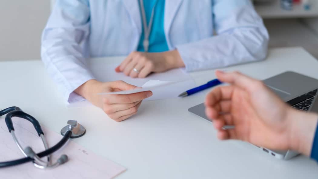 Mit diesen fünf Fragen finden Sie heraus, wie gut Ihr Arzt ist Unrecognizable doctor prescribing pills and drugs to patient. Male hand reaching for piece of paper with pharmacy recommendations. Symptom consultation and getting help