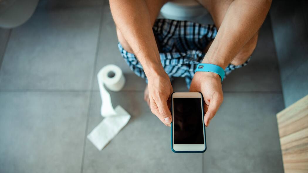 Nehmen Sie Ihr Smartphone nicht mit aufs WC! Close up of gentleman sitting on toilet bowl and holding smartphone stock photo