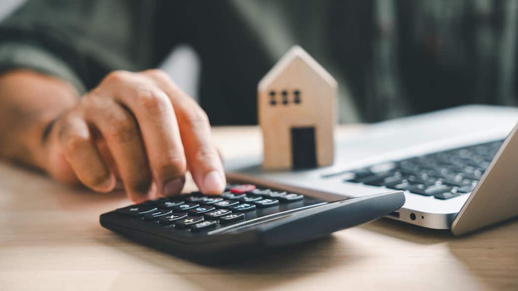 Festhypothek oder Saron? So hat sich die Ausgangslage geändert Pressing calculators, hand eyes home refinance. Wooden house model, buy/rent note on desk. Saving for property purchase concept, efficient mortgage payment. Tax, credit analysis for financial strategy