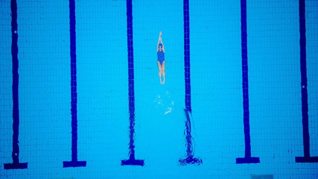Stiftung zahlt den Schwimmverein Female swimmer on evening training on swimming pool, warming up, swimming backstroke during training.