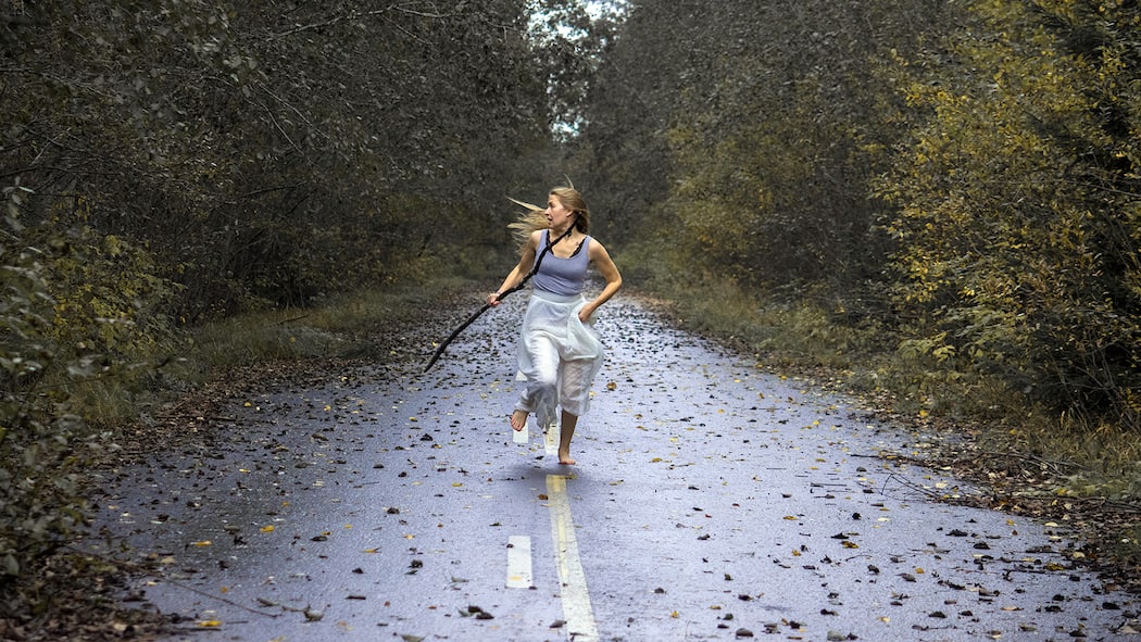 Ein dunkles Leben mit der Angst im Nacken Eine Frau rennt in Panik durch ein Waldstück. Sie hat einen Stock in der Hand.