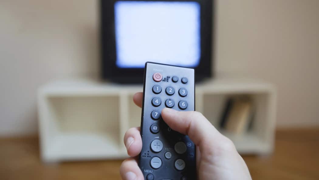 Sind wir von den Radio- und TV-Gebühren befreit? Eine Person hält eine Fernbedienung in der Hand. Im Hintergrund sieht man etwas verschwommen ein TV-Gerät.