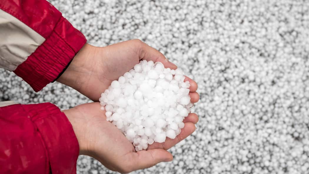 Hagelschäden? In diesen Fällen zahlt die Versicherung Eine Person hat Hagelkörner in der Hand - Unwetter mit Hagel führen oft zu Schäden an Autos, Gebäuden und Möbeln. Welche Versicherung springt ein, wenn etwas beschädigt wurde