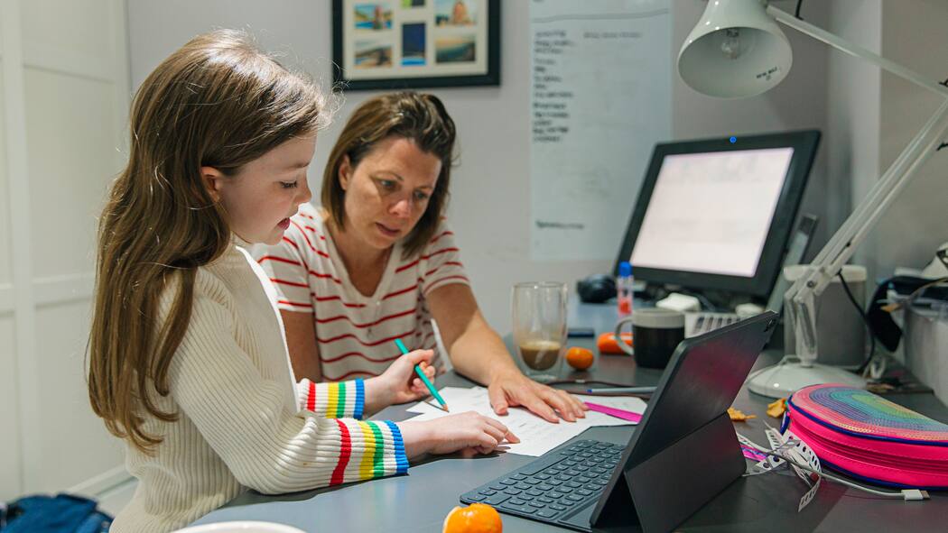 Die Kinder zu Hause unterrichten? Eine Mutter arbeitet im Homeoffice und kümmert sich nebenbei um ihre kleine Tochter, die ihre Schulaufgaben macht.