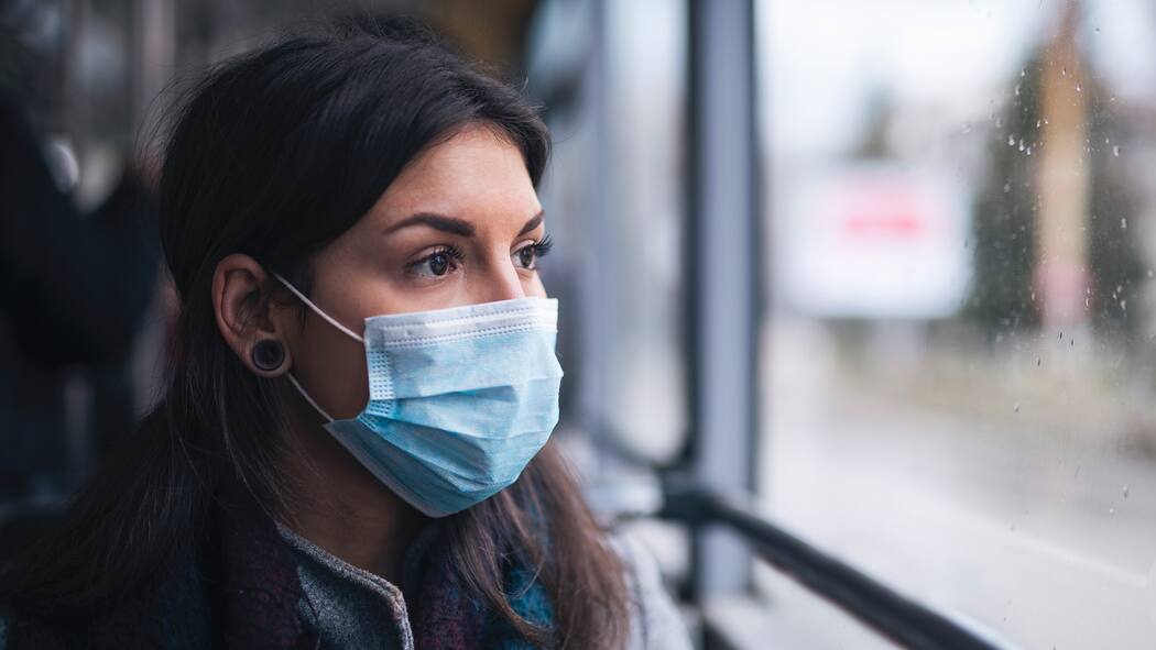 Die Pandemie belastet Junge psychisch mehr als Alte Frau mit Maske blickt nachdenklich aus Fenster