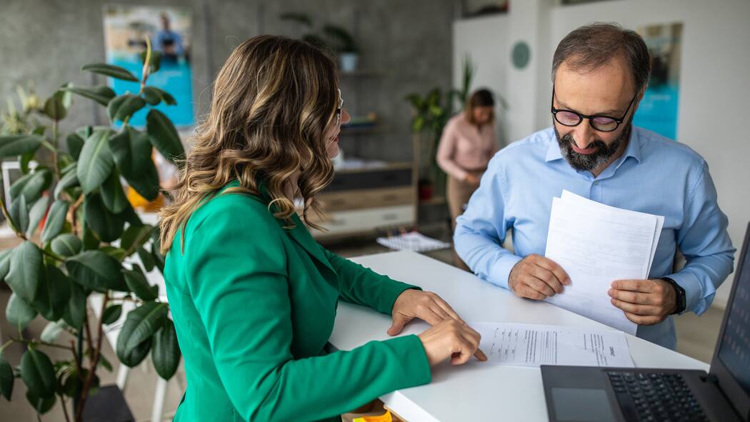 Wieso erbe ich die Säule 3a meiner Tante nicht? Eine Bankkundin steht am Bankschalter und lässt sich ihre Dokumente durch einen Angestellten prüfen.