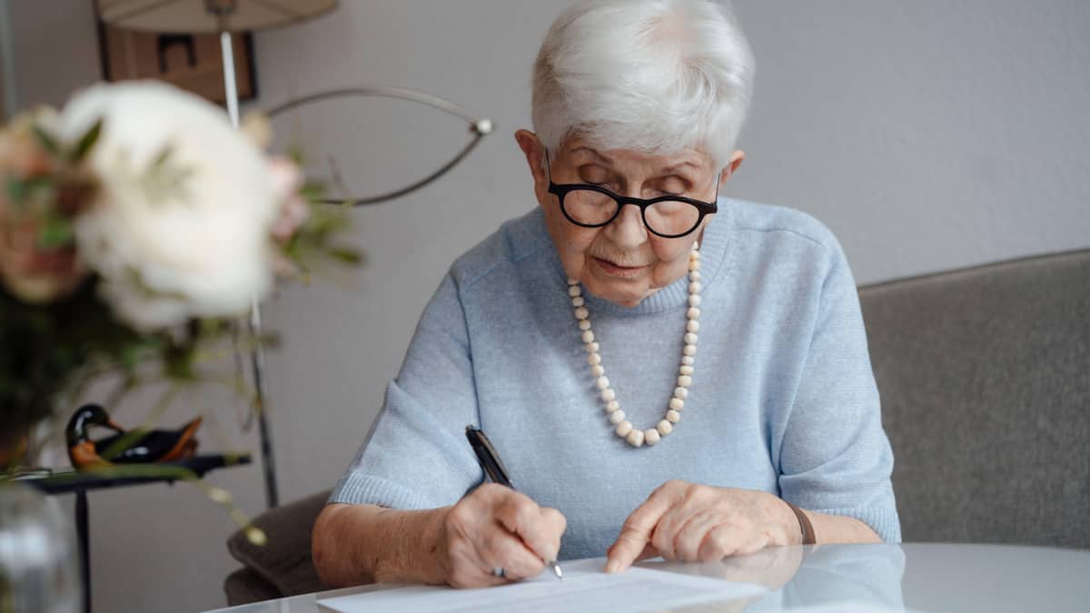 Seniorin schreibt auf einem Papier und sitzt zuhause am Tisch