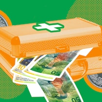 So sparen Sie bei den Prämien Ein Koffer mit Kreuz darauf und 50er-Banknoten darin vor Münzen und einem grünen Hintergrund - Der Beobachter gibt Tipps, wie Sie Ihre Gesundheitskosten bei der Krankenkasse aufgrund der gestiegenen Prämien senken können.