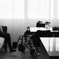 Den Betroffenen geht das Geld aus Anonyme Frau sitzt auf einem Sofa, vor ihr ein Rollstuhl. Auch zwei Jahre nach der Infektion leiden manche noch an Long Covid. Ihr Taggeld wird eingestellt, die IV lässt sich Zeit – jetzt kommt zur körperlichen noch die finanzielle Not.