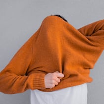 «Intuition hilft uns, rasch zu entscheiden» Unrecognisable man pulling cozy caramel sweater over his head on grey background. He is also wearing white t-shirt.