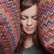 So krank macht uns ständiger Lärm Frau hält sich die Ohren mit Kissen zu - Der Alltagslärm nimmt zu – darunter leiden hochsensible Menschen besonders. Aber auch der Rest der Bevölkerung