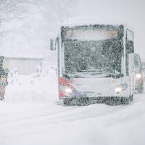Geld zurück, wenn das Wetter die Ferien vermiest? Bus im Schneegestöber. Snowboarder steigen ein.