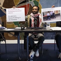 Rassismusvorwürfe: So reagiert die Polizei Mohamed Wa Baile an der Medienkonferenz zum neuen Urteil des EGMR. Er hält Plakate hoch, neben ihm zwei Juristinnen.