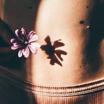 Analysen des Mikrobioms – was bringt das? Bauch einer jungen Frau mit einer Blume. In der Schweiz leiden Hunderttausende am schmerzhaften Reizdarmsyndrom. Labors bieten sinnlose Tests der Darmbakterien an.Was stattdessen helfen kann.