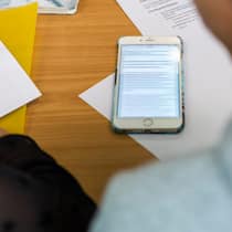 Ist künstliche Intelligenz als Prüfungshilfe erlaubt? Ein Smartphone liegt zwischen Zetteln auf einem Schultisch.