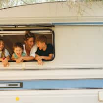 «Ewige» Schulferien – so vermeiden Sie eine Busse Eine Mutter und drei Kinder schauen lachend aus dem Fenster eines Wohnwagens.