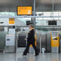 Flugpersonal streikt: Bekomme ich als Passagierin Geld? Eine Mitarbeiterin geht durch einen Flughafen, im Hintergrund sieht man Lufthansa-Schilder.