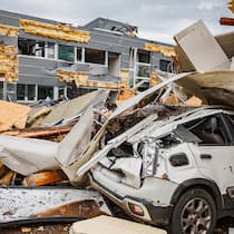 Auto- und Sachversicherungen werden deutlich teurer Zu sehen ist ein Gebäude, das von einem Sturm verwüstet wurde, die Fassade ist teilweise abgerissen. Davor sieht man ein zusammengebrochenes Gebäude und darunter begraben ein zerbeultes, weisses Auto.