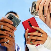 Jeder dritte Teenager nutzt KI-Tools wöchentlich Low angle view of three young people using mobile phones outdoors. Addicted gen z friends holding smartphone outside. Blue sky.