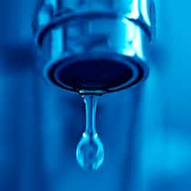 Wer muss die Reparatur bezahlen? Ein tropfender Wasserhahn vor blauem Hintergrund. Was rechtlich zum kleinen Unterhalt in der Mietwohnung zählt.