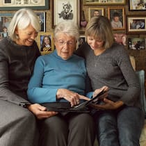 Junge wollen früher erben – ihre Eltern weigern sich Drei Frauen unterschiedlicher Generationen die auf einem Sofa ein Fotoalbum durchblättern.