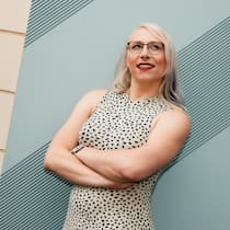 Endlich ich – eine trans Frau erzählt Die trans Frau Mia Macdonald trägt ein ärmelloses Kleid und steht selbstbewusst vor einer Wand. Sie lächelt und blickt nach rechts oben.
