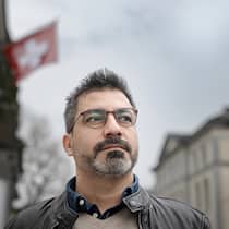 Justiz-Willkür? Thurgau ignoriert Bundesgericht Ein Mann mit Brille und kleinem Bart schaut an der Kamera vorbei, hinter ihm Häuser und eine Schweizerfahne.