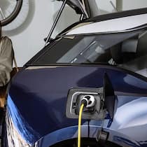 Zapfhahn in der Garage – worauf muss man achten? Mother and son pick up the groceries while electric vehicle is plugged in electric car charging station at home. Family housework. Energy Efficient, Sustainable domestic life. Vertical