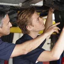 Zufrieden mit deiner Stifti? Ein Auto steht auf einer Hebebühne während zwei Mechaniker eine Inspektion durchführen.