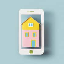 So erkennen Sie Fake-Angebote auf Buchungsplattformen Ein Handy mit einem Haus darin vor blauem Hintergrund. Nicht selten kommt es zu einem Betrug auf den verschiedenen Vergleichsplattformen.