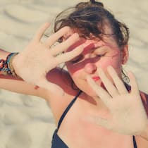Sonnenallergie – so schützen Sie sich Eine Frau am Strand hält die Hände schützend vor das Gesicht. Sonnenallergie betrifft oft Menschen mit heller Haut, insbesondere Frauen.