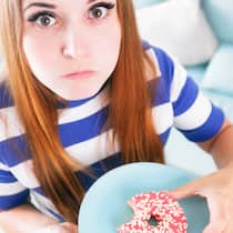 Habe ich eine Essstörung? Eine junge Frau isst einen Donut und hat dabei Schuldgefühle. Leidet sie unter einer Essstörung?