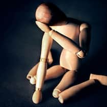 So gehen Sie mit der Invalidenversicherung um Eine Holzfigur kniet am Boden und hält verzweifelt seinen Kopf.