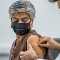 Wie gut und wie lange schützt die Corona-Impfung? Frau mit Schutzmaske bekommt Pflaster auf den Arm nach Corona-Impfung