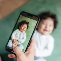 Kinderfotos posten? Die Folgen können gravierend sein Frau macht mit Handy einen Schnappschuss von einem Kind - Ein Lächeln auf Facebook, Konsequenzen Jahre später. Was Eltern über die Langzeitfolgen von Kinderfotos online wissen sollten