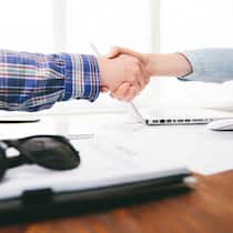 Hoppla, ist das jetzt ein Vertrag? Zwei Personen sitzen an einem Schreibtisch und geben sich zum Zeichen des Vertragsschlusses die Hand.