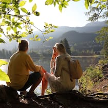 Mit 55 raus aus dem Job? So viel Kapital brauchen Sie Ein älteres Paar sitzt in an einem See - Früher aufhören zu arbeiten gilt als Inbegriff von Freiheit. Doch zwischen Theorie und Realität klafft eine Lücke von Millionen. Wir zeigen, mit welchen Summen Sie tatsächlich rechnen müssen