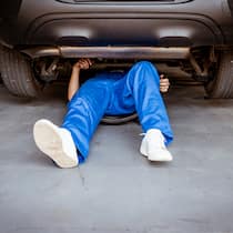 Eine Garage verlangt achtmal mehr als die andere Ein Automechaniker in blauer Arbeitsuniform liegt unter einem Auto, das er gerade am Reparieren ist. Bei Offerten zu Autoreparaturen ist es wichtig, mehrere zu vergleichen, selbst wenn man wegen der Autoversicherung an eine Partnergarage gebunden ist.