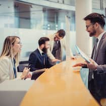 Warum die Bank sich beim Erben querstellt Eine Bankangestellte spricht mit einem Kunden, der am Tresen vor ihr steht.