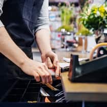 So können Sie Liquidität beschaffen Ein Florist legt Bargeld in seine Registrierkasse.