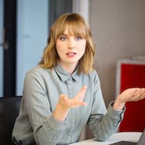 Ist es Zeit für eine Sanierung – oder für den Konkurs? Geschäftsfrau diskutiert an einem geschäftlichen Termin. Sie gestikuliert mit den Händen.