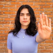 Sie sind nicht machtlos gegen Gewalt Eine junge Frau steht vor einer Mauer und streckt ihre Hand aus, mit der Handfläche Richtung Kamera.